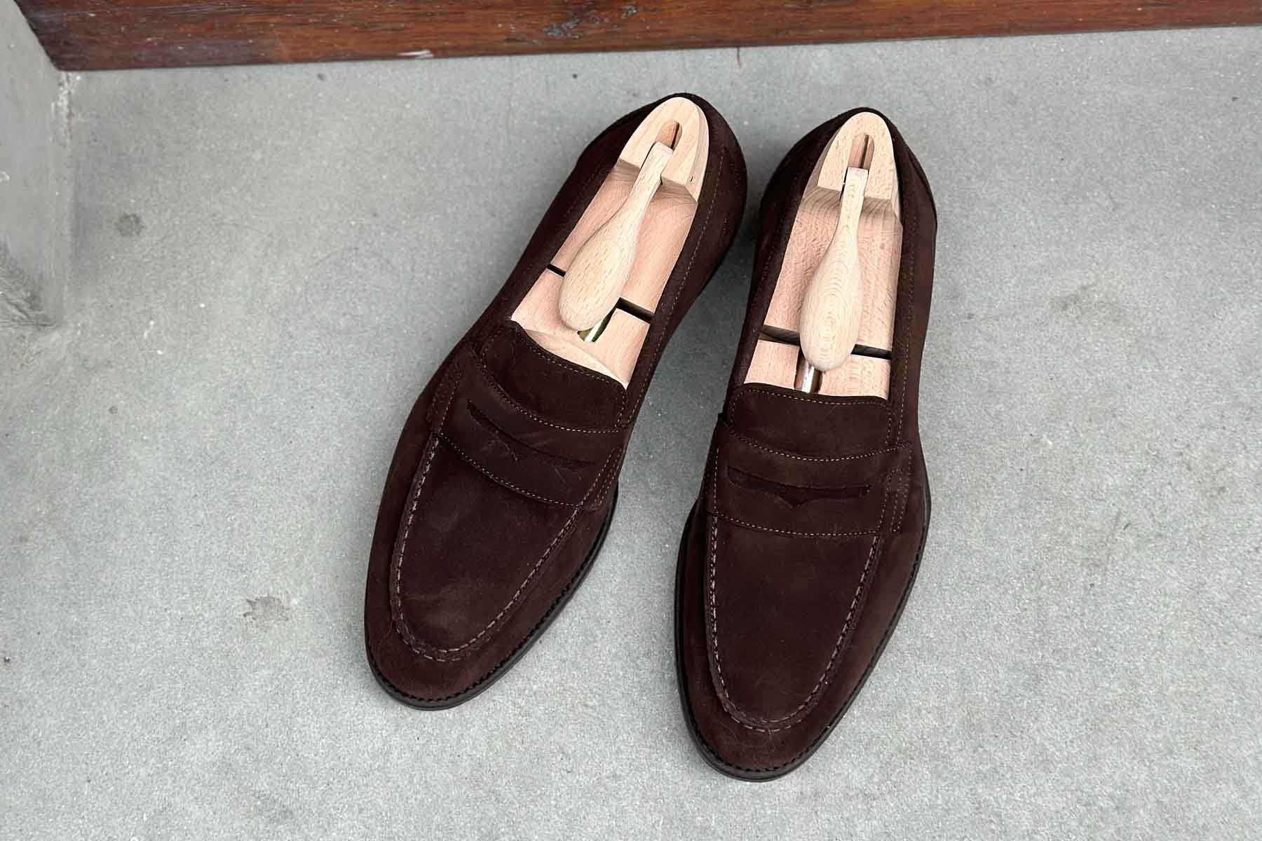 Carlos Santos 9176 Elliot unlined dark brown suede Penny Loafers with soft-chiseled toe and leather sole on gray background.